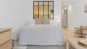 Een moderne slaapkamer met een groot bed, nachtkastjes, een spiegel en uitzicht.