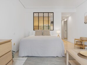 A modern bedroom with a large bed, bedside tables, a mirror, and a view of the outside. - Confortable Estudio en Medina Garden ref 332 (Marbella)