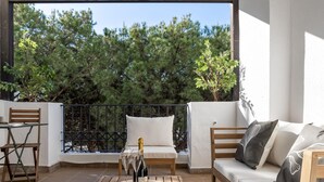 Een balkon met een houten tafel, twee stoelen, een bank en een fles champagne.