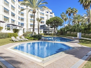 A hotel with a swimming pool, palm trees, and a clear blue sky. - Amplio y Luminoso Apartamento en Las Gaviotas (Marbella)