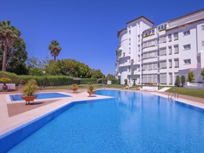 A large swimming pool with multiple lounge chairs and planters, surrounded by a white building with balconies. - Amplio y Luminoso Apartamento en Las Gaviotas (Marbella)