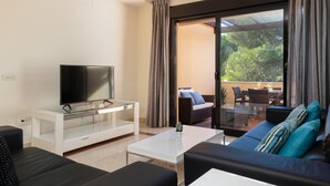 A modern living room with a flat-screen TV on a glass table, a sofa, and a balcony with outdoor furniture. - Mimosas de Ban s (Marbella)