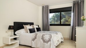 A bedroom with a bed, bedside table, lamp, and a window with curtains. - Mimosas de Ban s (Marbella)