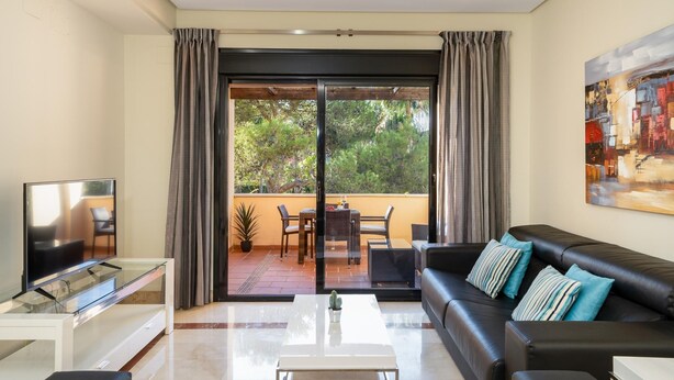 A modern living room with a black leather sofa, a glass coffee table, and a flat-screen TV on a white stand. - Mimosas de Ban s (Marbella)
