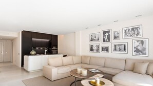 A modern living room with a beige sectional sofa, a round coffee table with candles, and a kitchen area with dark cabinets. - 2 Dormitorios Playas del Duque Ref 228 (Marbella)