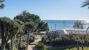A coastal view with a pathway leading to a building, surrounded by palm trees and a clear sky. - 2 Dormitorios Playas del Duque Ref 228 (Marbella)