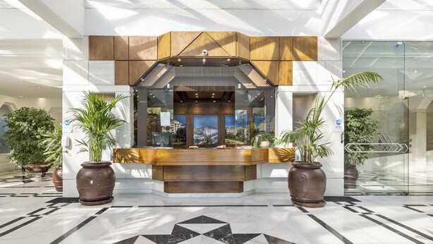 A reception area with a modern design, featuring a reception desk, potted plants, and a geometric floor pattern. - Elegante Apartamento en Las Gaviotas (Marbella)