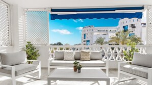A balcony with a white outdoor seating area, a table, and a view of a building with the sign 'VAS-DUQUE'. - Elegante Apartamento en Las Gaviotas (Marbella)