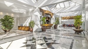 A spacious lobby with a geometric floor pattern, a reception desk, and multiple potted plants. - Elegante Apartamento en Las Gaviotas (Marbella)