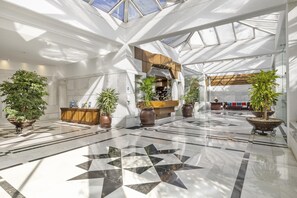 A spacious lobby with a geometric floor pattern, a reception desk, and multiple potted plants. - Elegante Apartamento en Las Gaviotas (Marbella)