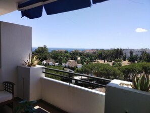 A balcony with a view of a coastal town, a chair, and potted plants. - Estudio en Medina Garden Ref 362 (Marbella)