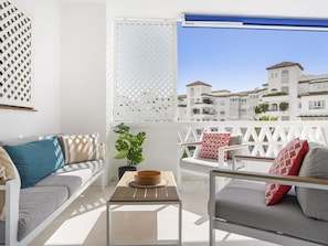 Ein Balkon mit weißem Gitter, einer Couch, einem Sessel und einem kleinen Tisch mit einer Schale.