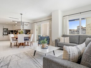 Ein modernes Wohnzimmer mit grauem Sofa, einem Couchtisch und einem Essbereich mit Tisch und Stühlen.