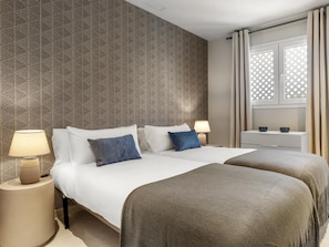 Ein Hotelzimmer mit zwei Betten, einem Nachttisch mit Lampe, einem Schminktisch und einem Fenster mit Vorhängen.