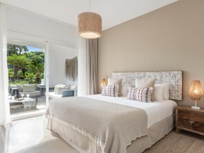 A bedroom with a large bed, a wooden nightstand, a hanging light fixture, and a view of a balcony with outdoor furniture. - Fant Stico Apartamento en Jardines de Ventura (Marbella)