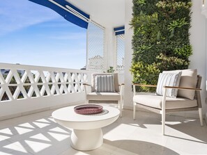A balcony with a white lattice railing, two white chairs with cushions, a round white table, and a vertical garden wall. - Espacioso y Encantador Apartamento en Las Gaviotas (Marbella)