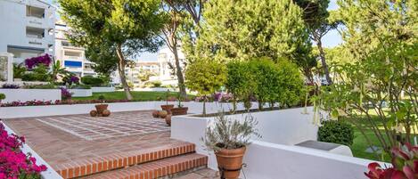 Une cour avec une terrasse carrelée, des plantes en pot et un bâtiment blanc en arrière-plan.