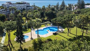 Un resort con una piscina grande rodeada de exuberante vegetación y vistas al mar.