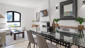 Una sala de estar moderna con una mesa de comedor de vidrio, sillas grises, un sofá, una mesa de centro y un televisor montado en la pared.