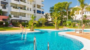 Ein Pool mit geschwungener Kante, umgeben von einer Grünanlage mit Palmen und einem mehrstöckigen Gebäude im Hintergrund.