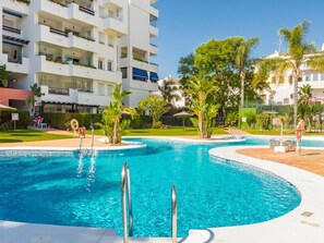 Ein Pool mit geschwungener Kante, umgeben von einer Grünanlage mit Palmen und einem mehrstöckigen Gebäude im Hintergrund.