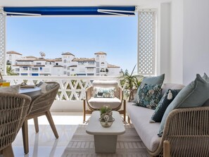 Ein Balkon mit Korbmöbeln, einem weißen Sofa und Blick auf weiße Gebäude mit roten Dächern.