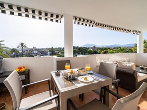 A balcony with a table set for breakfast, including fruits, bread, and orange juice. - Apartamento en Playa Roc o (Marbella)