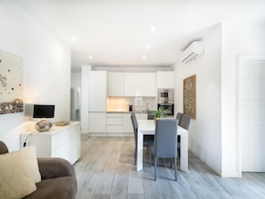 A modern kitchen with white cabinets, a dining table with chairs, and a coffee machine. - Vista Piscina en Andaluc a del Mar (Marbella)