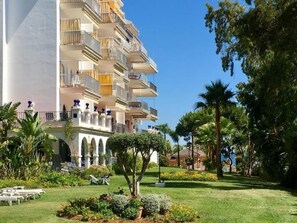 A multi-story hotel with balconies, a garden with palm trees, and outdoor seating. - Vista Piscina en Andaluc a del Mar (Marbella)