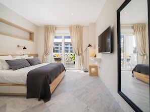 Ein modernes Schlafzimmer mit Bett, Fernseher und einem Balkon mit Blick auf Gebäude.