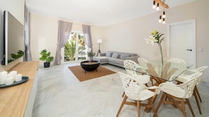 Ein modernes Wohnzimmer mit einer Couch, einem Esstisch mit Stühlen, einem Fernseher und einem Balkon mit Vorhängen.