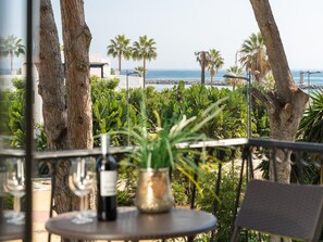 Ein Balkon mit Tisch, einer Flasche und einer Pflanze, mit Blick auf einen Strand mit Palmen und das Meer.