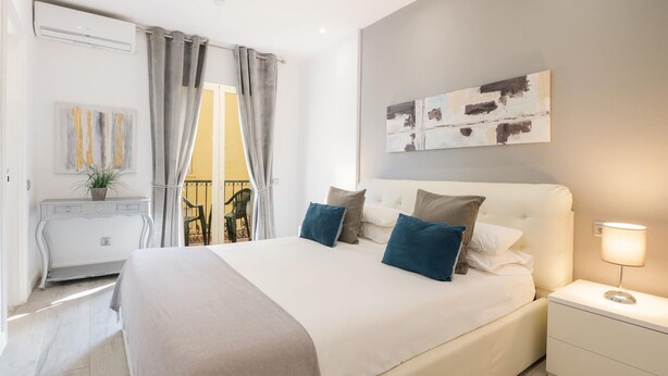 Quarto moderno com uma cama grande, mesas de cabeceira, um criado-mudo, ar condicionado na parede e uma varanda com vista.