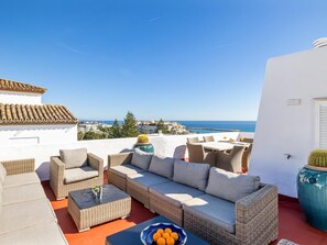 Eine Dachterrasse mit Korbmöbeln, einem Tisch mit Orangen und Blick auf das Meer.