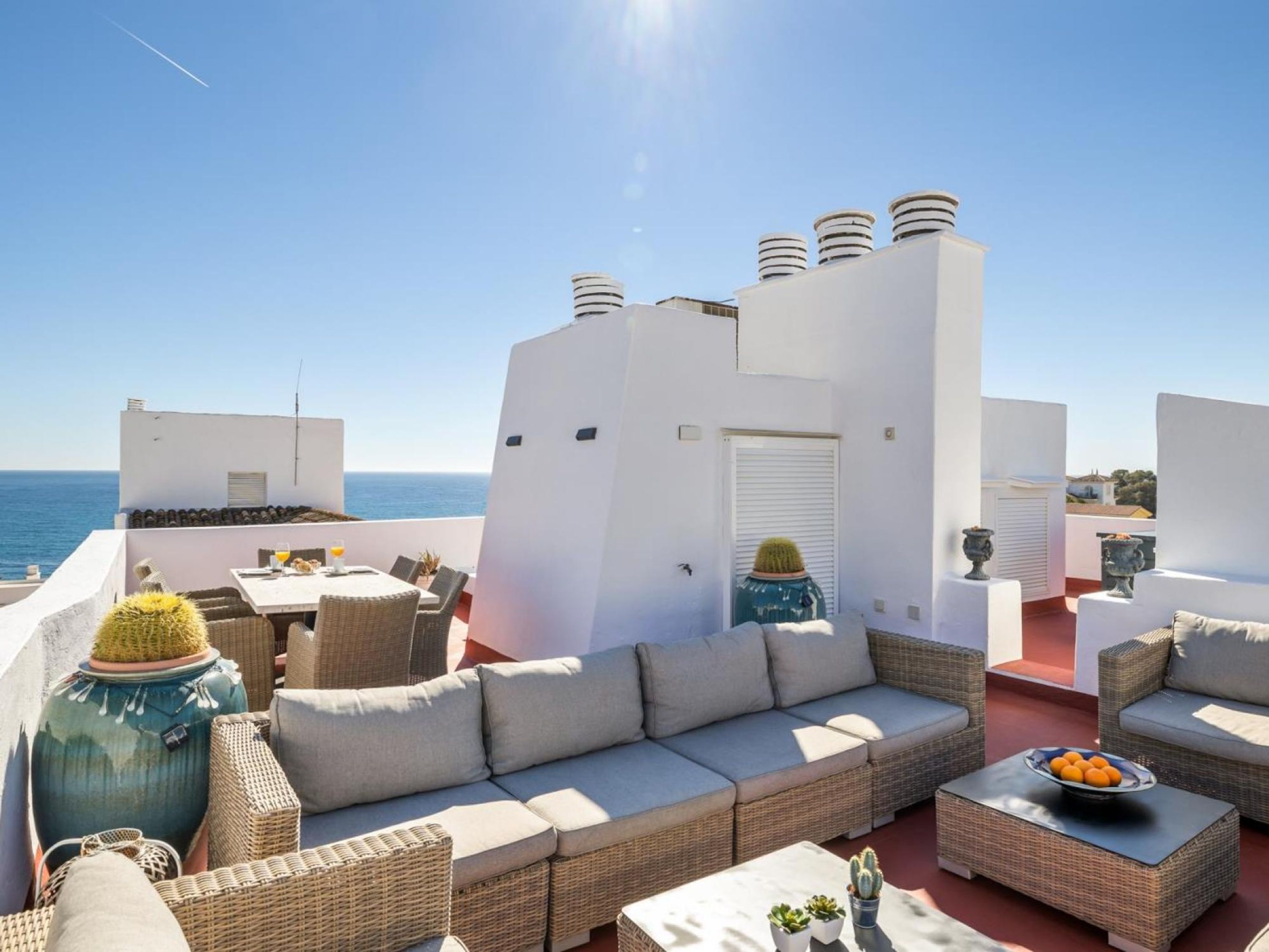 Eine Dachterrasse mit einer Sofagruppe, einem Esstisch und Blick auf das Meer.