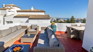A rooftop terrace with outdoor furniture, a large vase, and a view of buildings and the sea. - Casa C diz 607 Playas del Duque (Marbella)