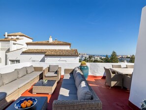 Eine Dachterrasse mit Gartenmöbeln, einer großen Vase und Blick auf Gebäude und das Meer.