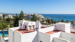 A coastal residential area with white buildings, a clear blue sky, and a view of the sea. - Casa C diz 607 Playas del Duque (Marbella)