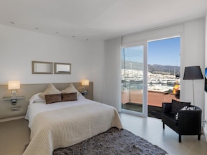 Ein Hotelzimmer mit einem Bett, zwei Nachttischlampen, einem Sofa, einem großen Fenster mit Blick auf einen Yachthafen und einem Balkon.