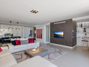 Ein modernes Wohnzimmer mit einem weißen Sofa, einem Couchtisch und einem an einer dunklen Wand befestigten Fernseher.