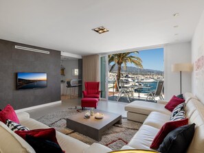 Ein modernes Wohnzimmer mit großem Fenster mit Blick auf einen Yachthafen und Berge.