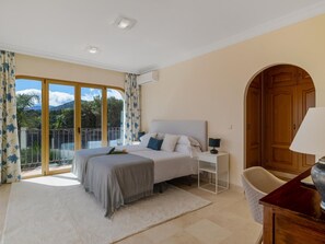 A bedroom with a bed, a nightstand, a chair, a wooden door, and a view of the outdoors. - Villa Los Arqueros Golf (Benahavis)