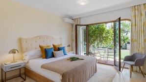 Ein Schlafzimmer mit einem großen Bett, einem Nachttisch, einer Lampe und Blick ins Freie durch eine Schiebetür.