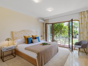 A bedroom with a large bed, a bedside table, a lamp, and a view of the outdoors through a sliding glass door. - Villa Los Arqueros Golf (Benahavis)