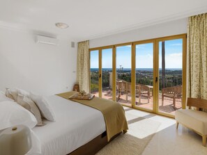 A hotel room with a large bed, a wooden bench, and a balcony with a view of the landscape. - Villa Los Arqueros Golf (Benahavis)