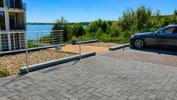 Ein Parkplatz mit befestigter Fahrbahn, ein Auto und ein Gebäude mit Balkon mit Blick auf ein Gewässer.