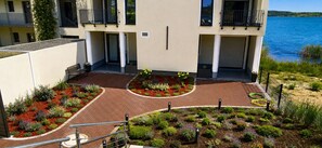 A courtyard with a brick pathway, surrounded by landscaped gardens and a body of water. - 120-square-meter vacation rental with lake views, dock right on the water / Sleeps 8, 3 bedrooms (Neukieritzsch)