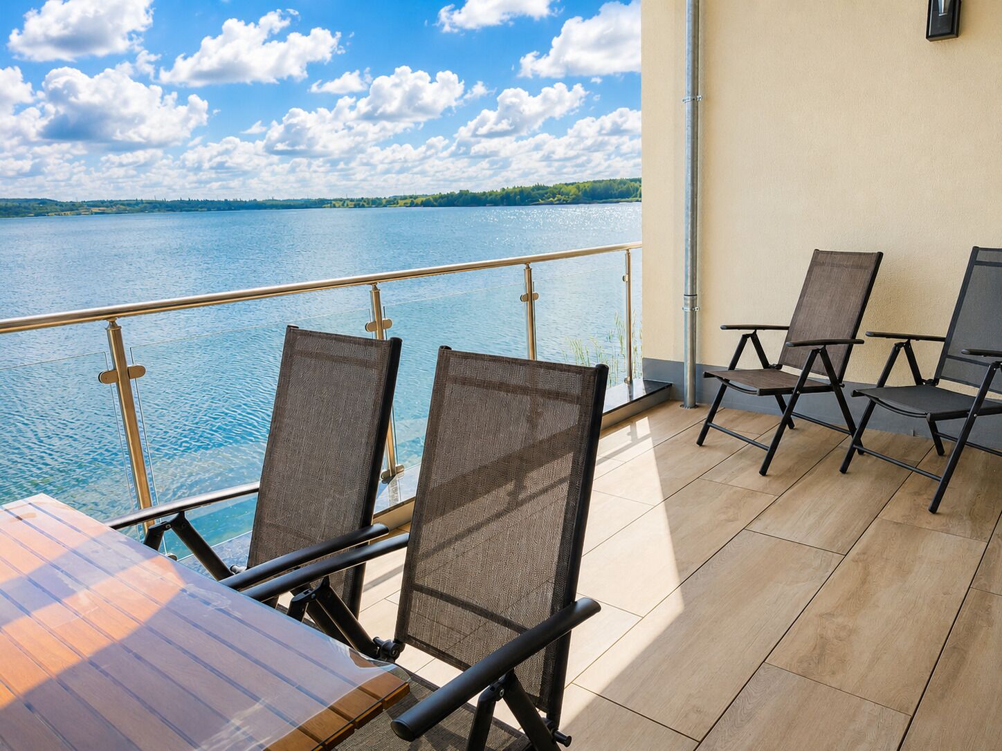 A balcony with a view of a lake, equipped with chairs and a table.