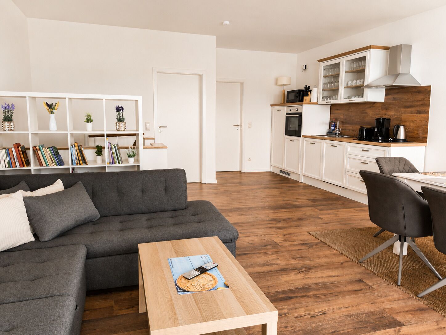 A modern living room with a grey sofa, a wooden coffee table, and a bookshelf filled with books and decorative items.