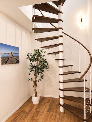 A spiral staircase with white railings and wooden steps, a potted plant, and a framed picture on the wall. - 120-square-meter vacation rental with lake views, dock right on the water / Sleeps 8, 3 bedrooms (Neukieritzsch)